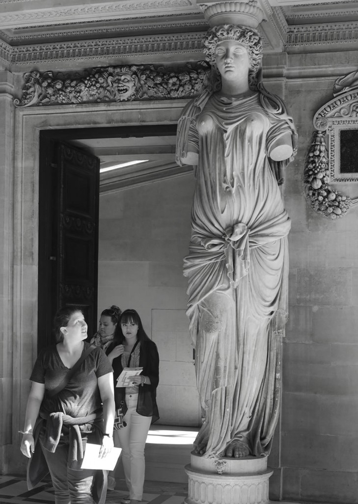 Visitors entering the Caryatid room at the Louvre, whose doorway is flanked by four female figures (the caryatids: female figures serving as architectural support) sculpted by Jean Goujon in 1550.