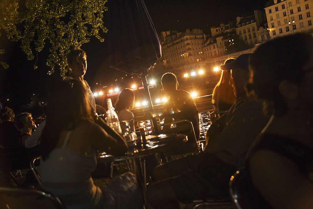 Sitting along the Seine at Paris Plages, the moment that the Bateaux Mouches tourist boats ride by, shining light into all the shadows as it passes. 