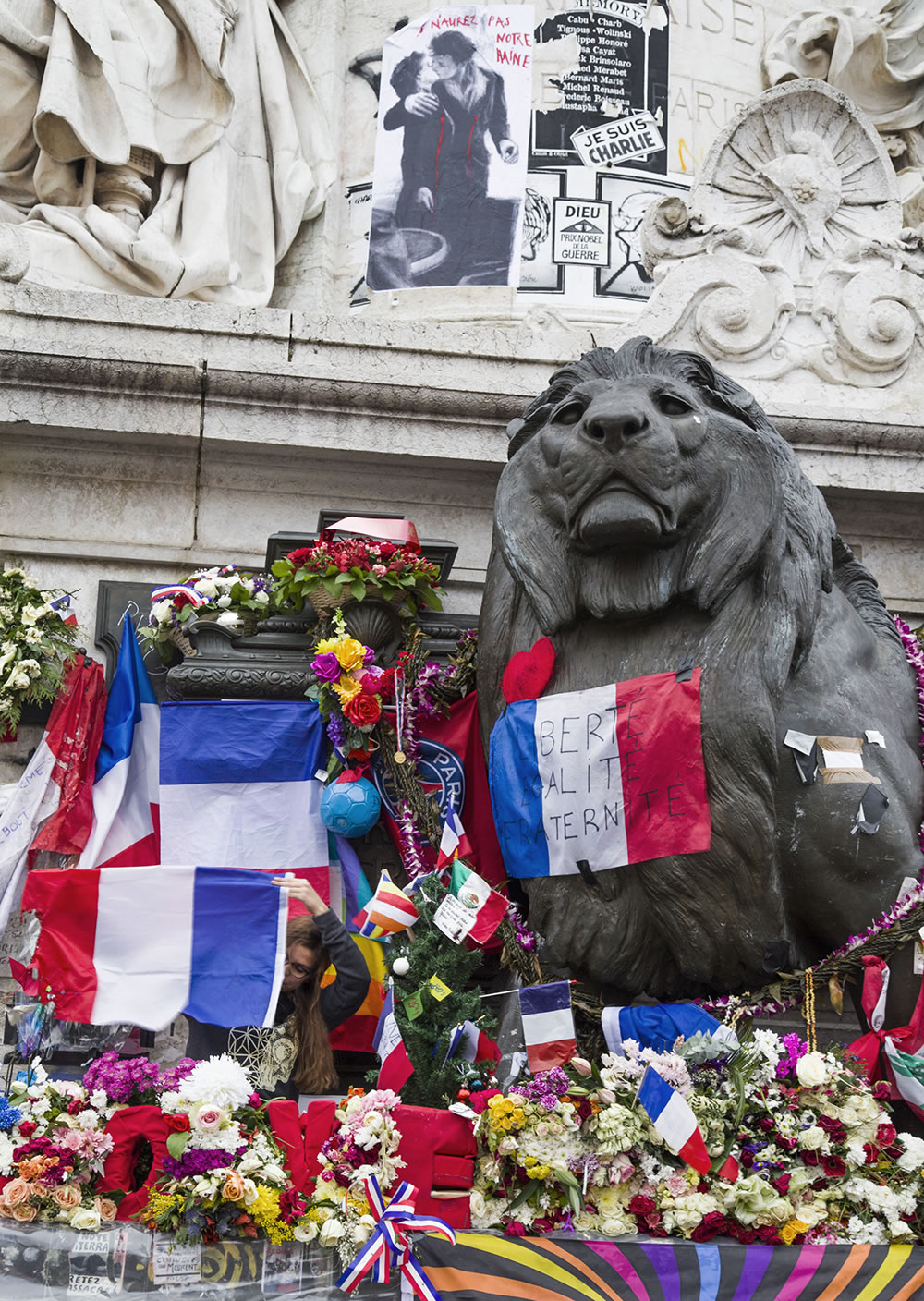 A young woman inspects a French flag on the collective memorial in the center of Place de la République, Paris.  The memorial was damaged on Sunday during conflict between police and protesters.
